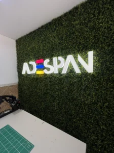 Letreiro luminoso em acrilico da Adespan com iluminação LED branca e detalhes coloridos instalado em parede de jardim vertical.
