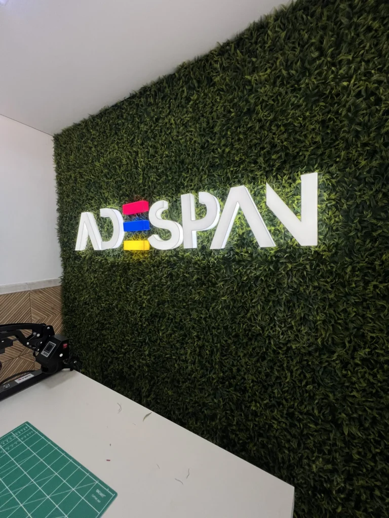 Letreiro luminoso em acrilico da Adespan com iluminação LED branca e detalhes coloridos instalado em parede de jardim vertical.